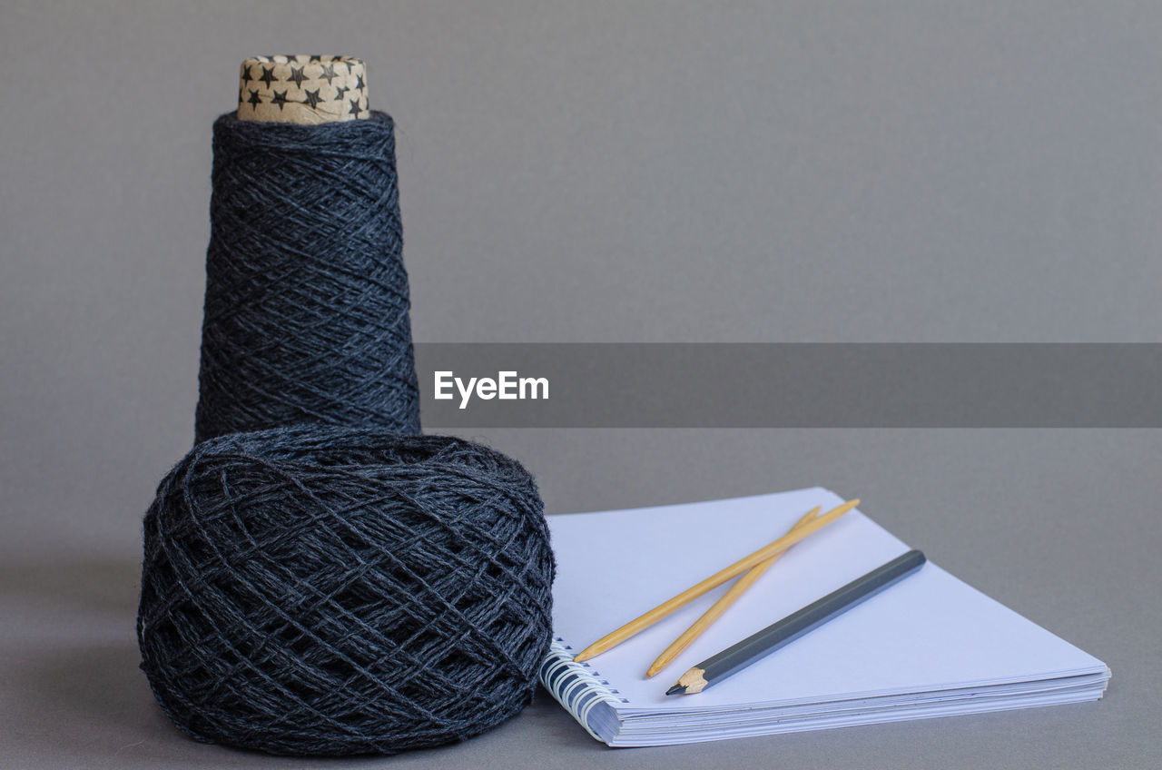 Cone and ball of gray wool, knitting bamboo needles, notebook and gray pencil on gray background. 