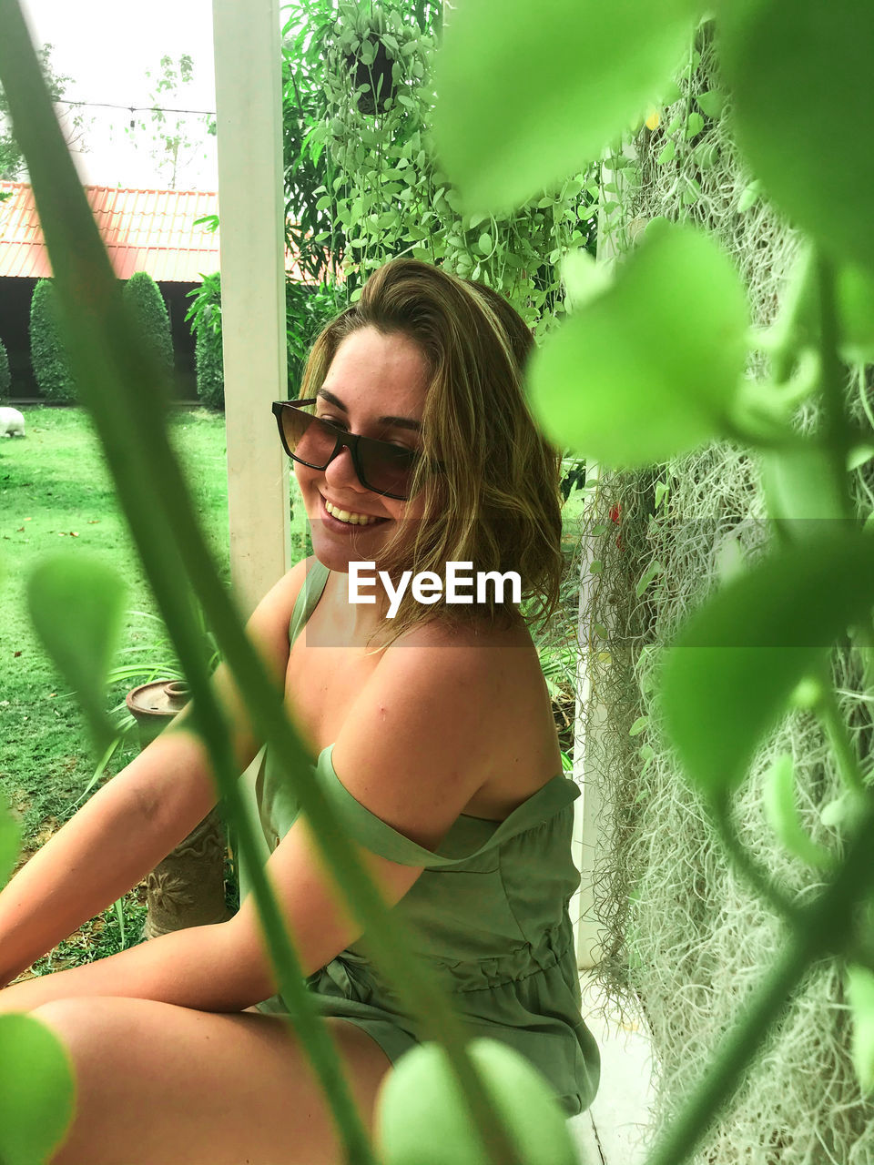 Smiling woman wearing sunglasses sitting by plants