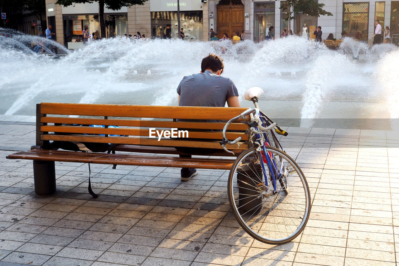 REAR VIEW OF MAN CYCLING ON CITY IN BACKGROUND