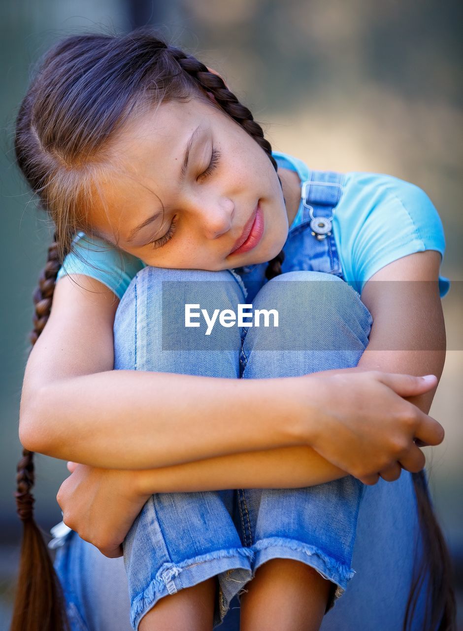 Close-up of girl hugging knees outdoors