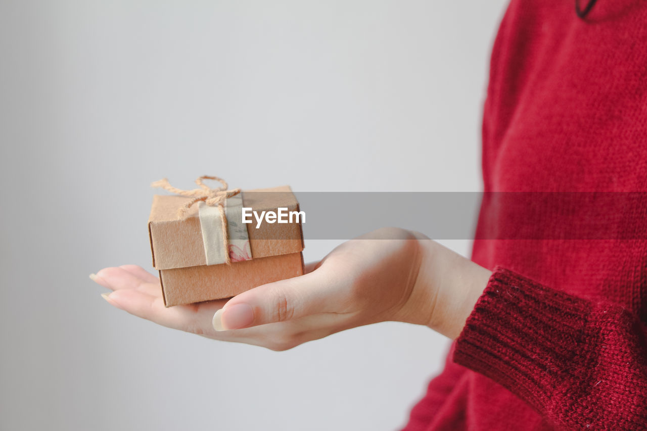 cropped hand of woman holding gift box against white background