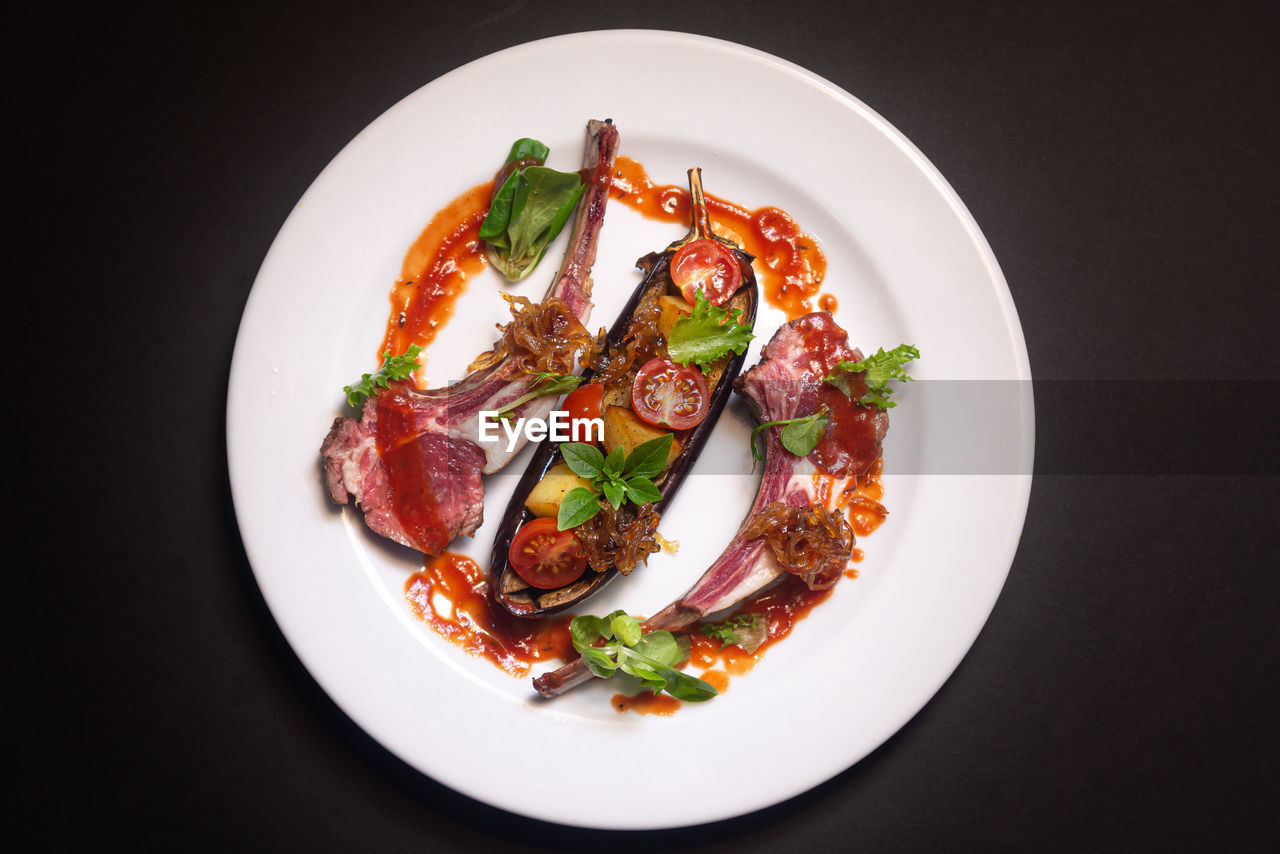 Lamb ribs fried, baked eggplant, cherry tomatoes, fried onions, basil, red sauce. view from above.
