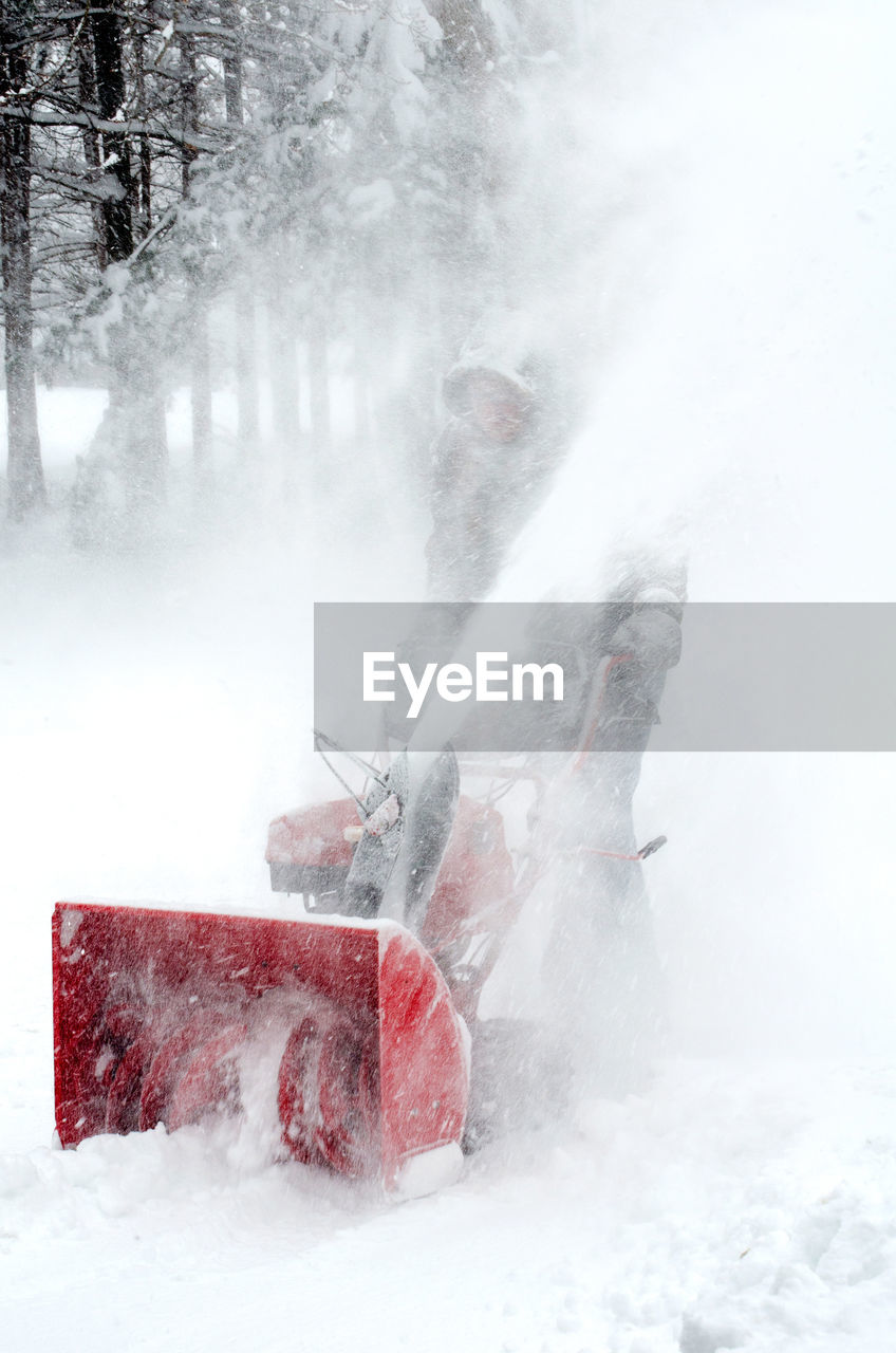 Male worker is covered in snow, as he walks behind a snow blower