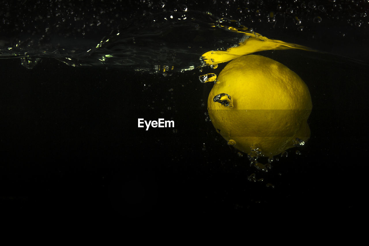 Close-up of lemon floating in water against black background