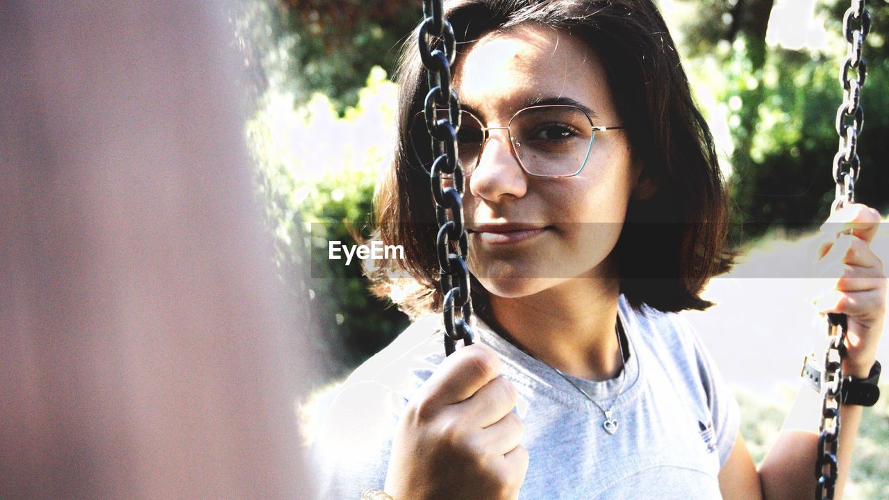 Close-up portrait of girl holding chain while sitting on swing