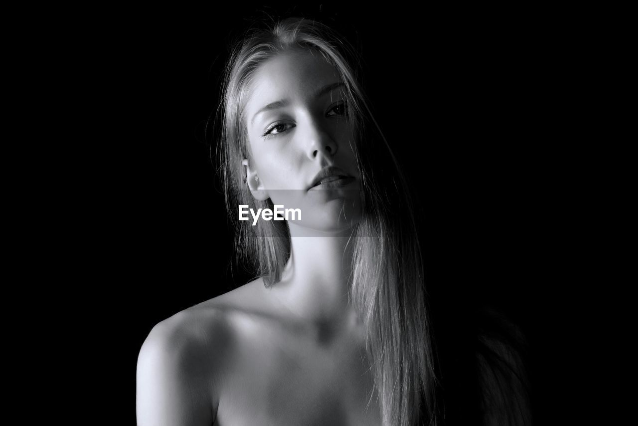 CLOSE-UP OF YOUNG WOMAN AGAINST BLACK BACKGROUND