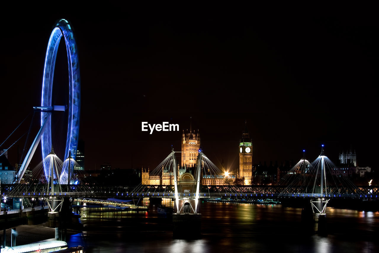Illuminated bridge over thames river by millennium wheel in city against clear sky at night