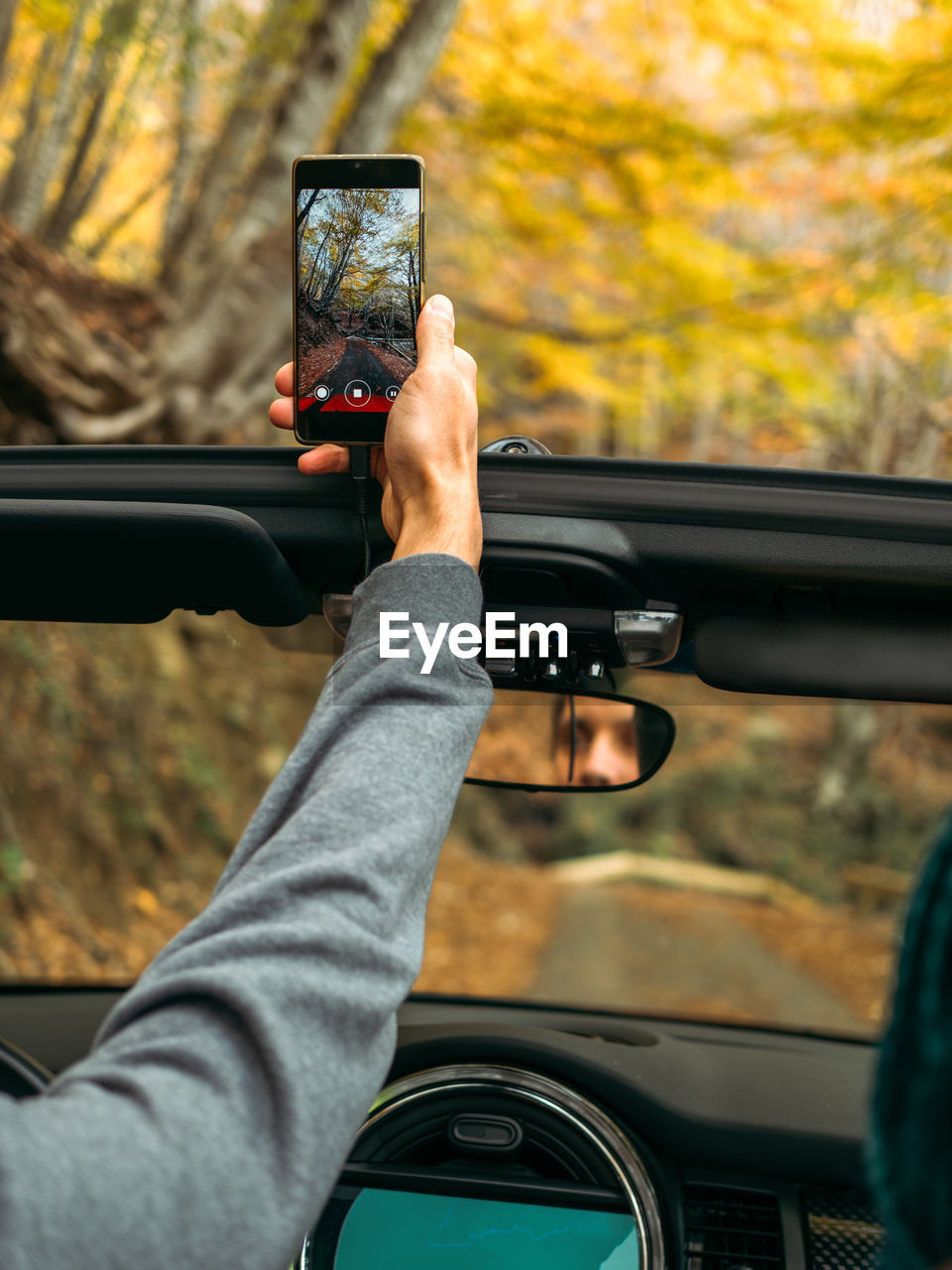 Man takes a vertical video on a mobile phone from the car on the road in the autumn beautiful forest