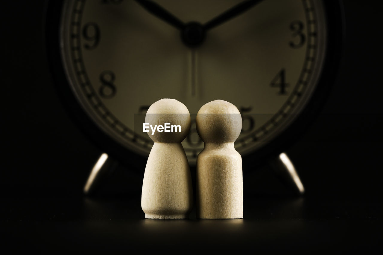 Couples of wooden peg dolls over dark background with an alarm clock