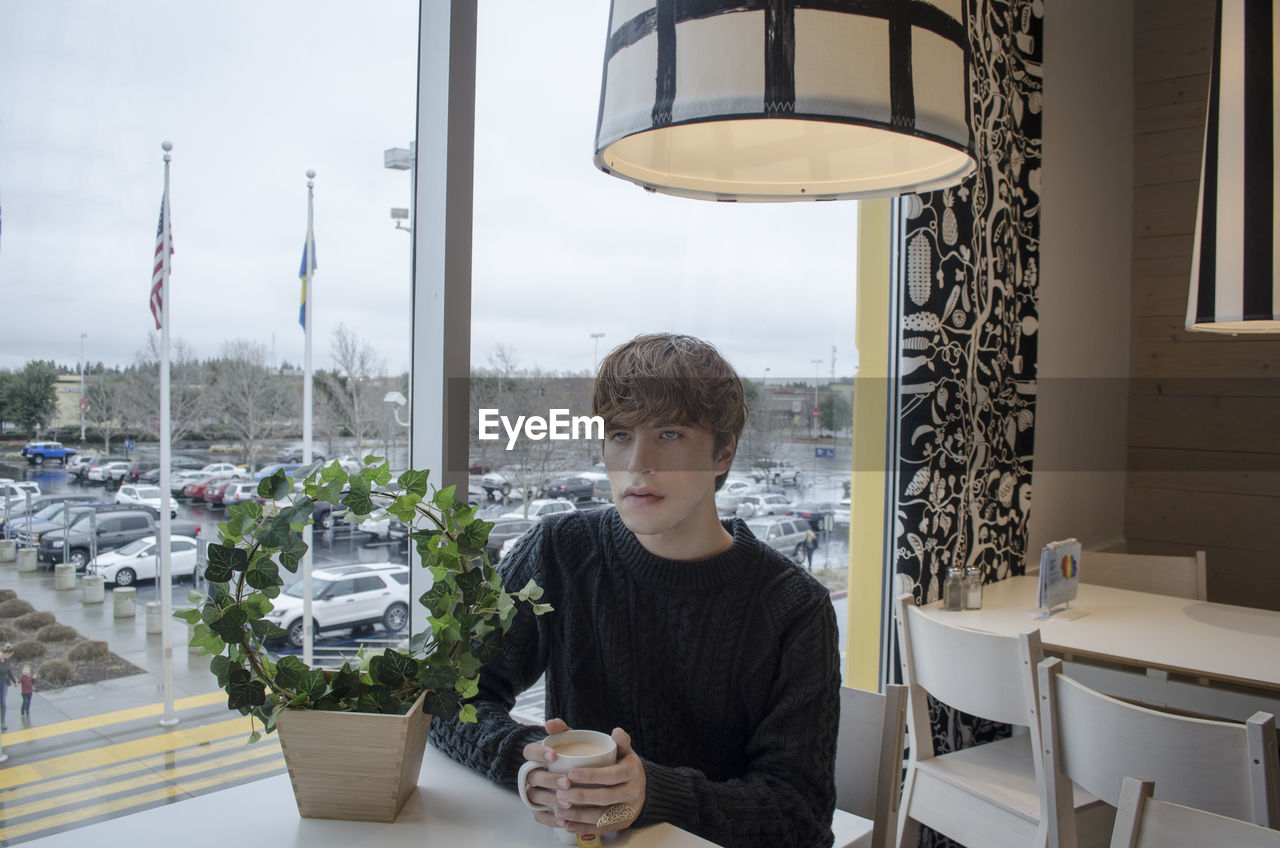 Young man with coffee looking away while sitting in cafe