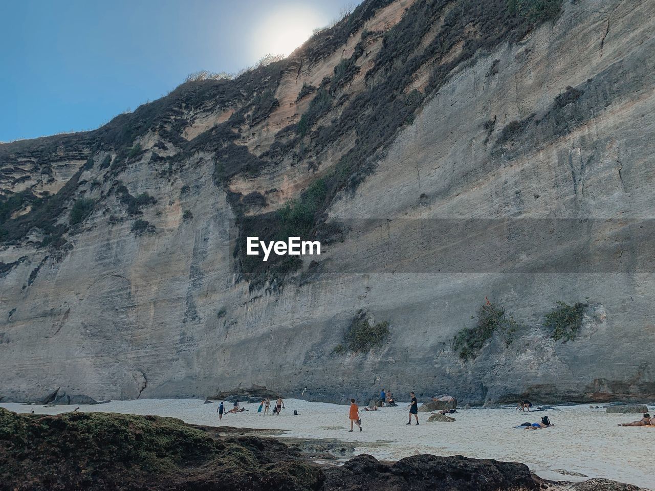 People relaxing on beach against rock mountain and sky