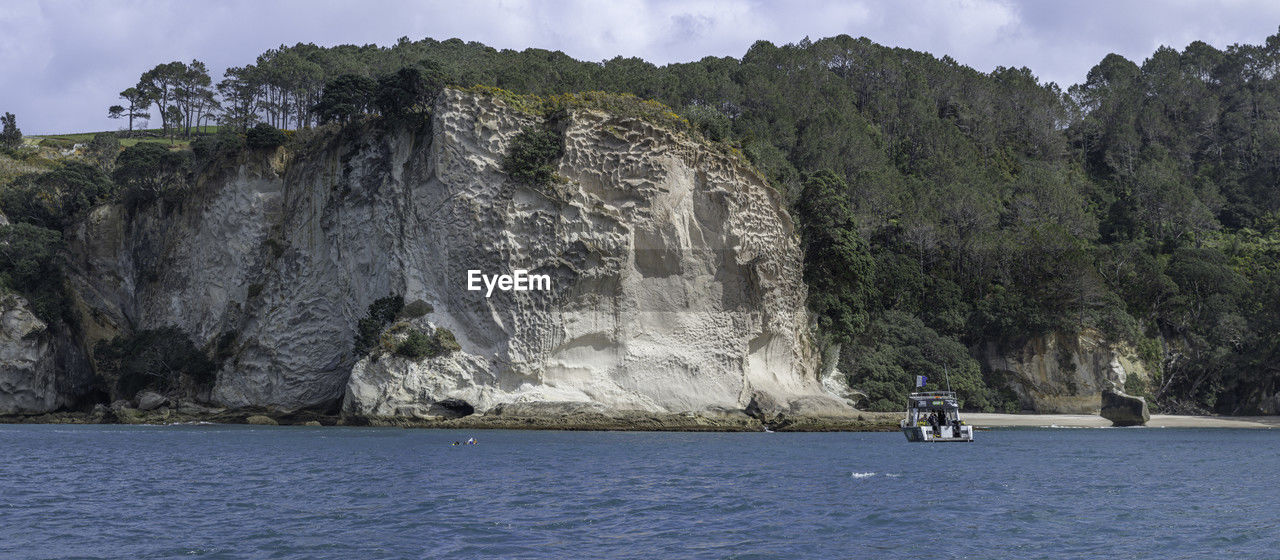 Scenic view of tall cliffs facing the sea against sky with scuba divers and boat