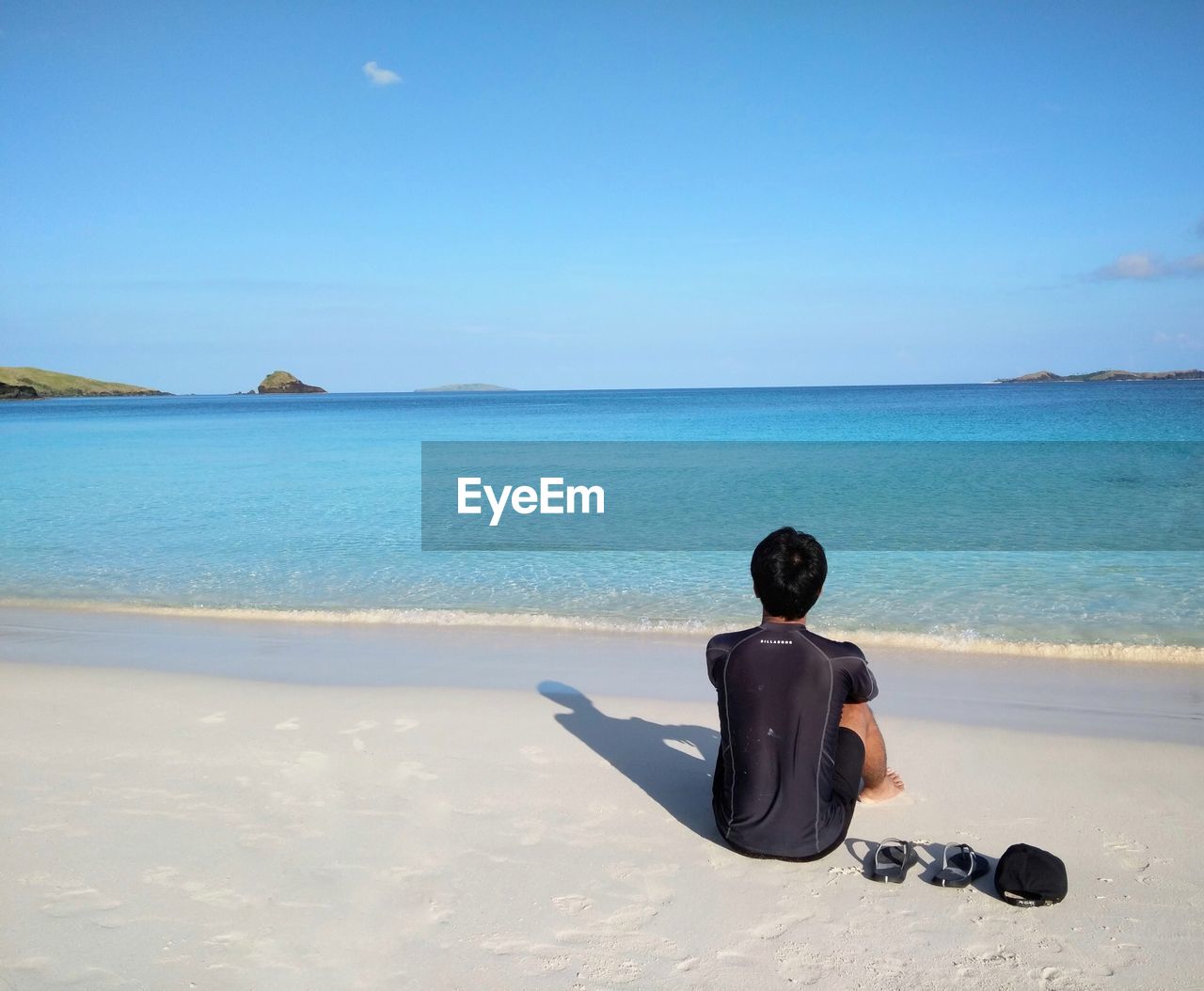 Rear view of man sitting on shore at beach against sky