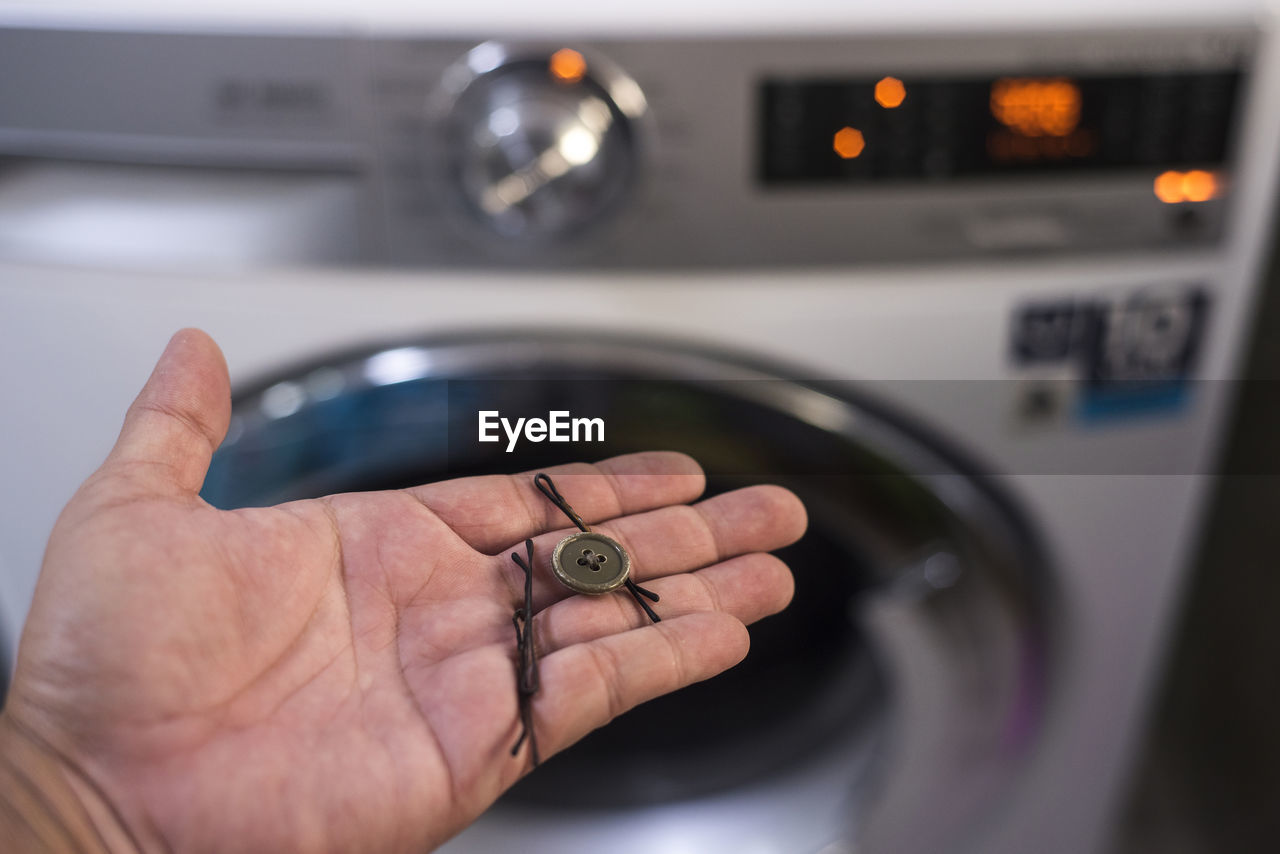 Cropped hand holding button and hairpins against washing machine