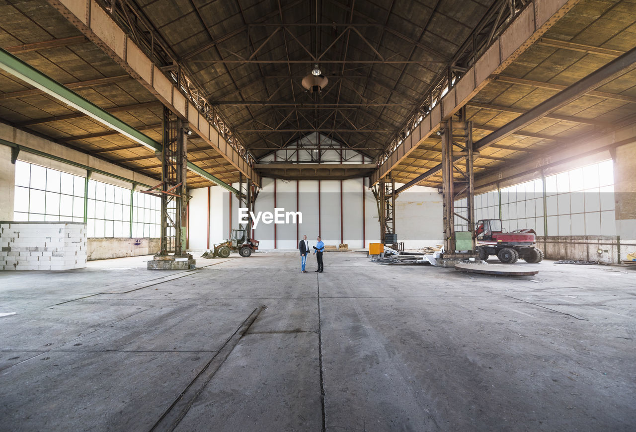 Two businessmen with documents talking in old industrial hall