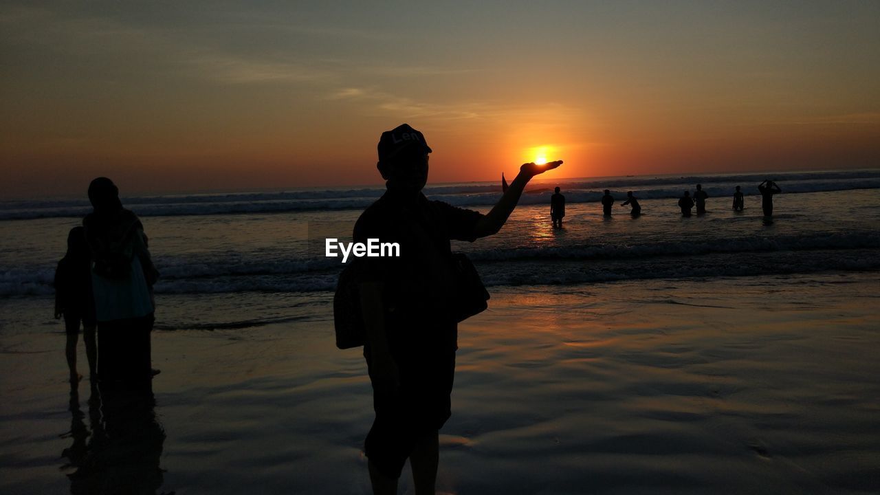 Optical illusion of silhouette man holding sun at beach