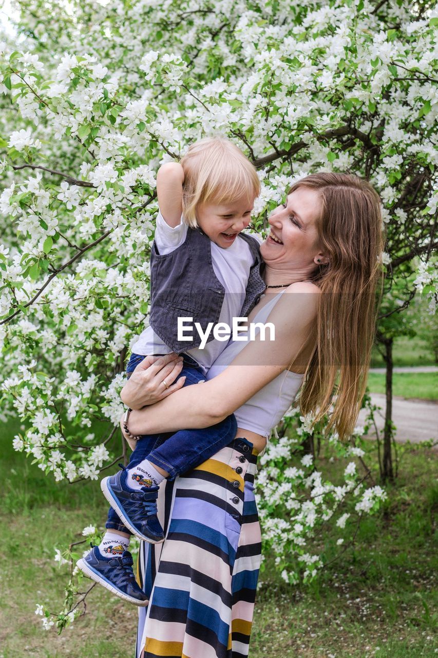 Young smiling mother with son in apple tree garden. 