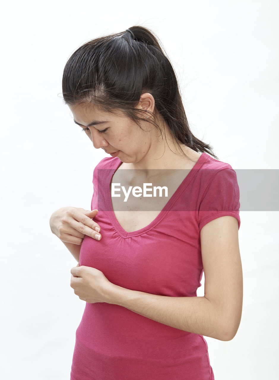 Woman touching breast while standing against white background