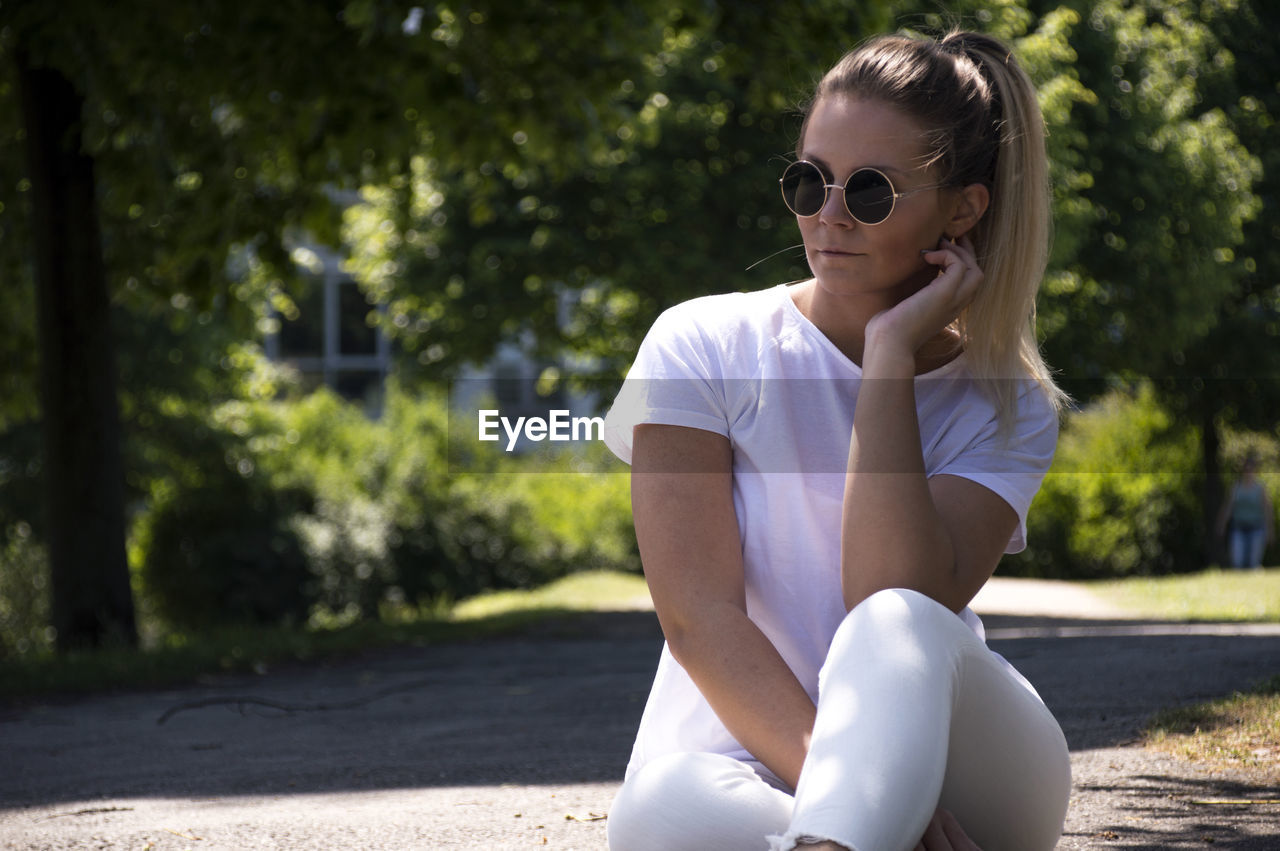 Young woman wearing sunglasses while sitting on walkway at park