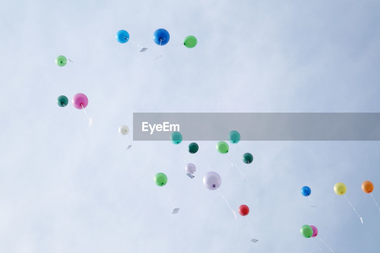 Low angle view of colorful helium balloons flying against sky