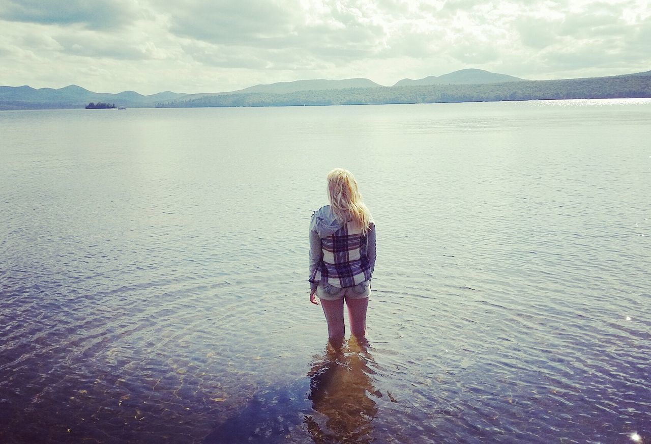 Rear view of woman standing in lake against sky