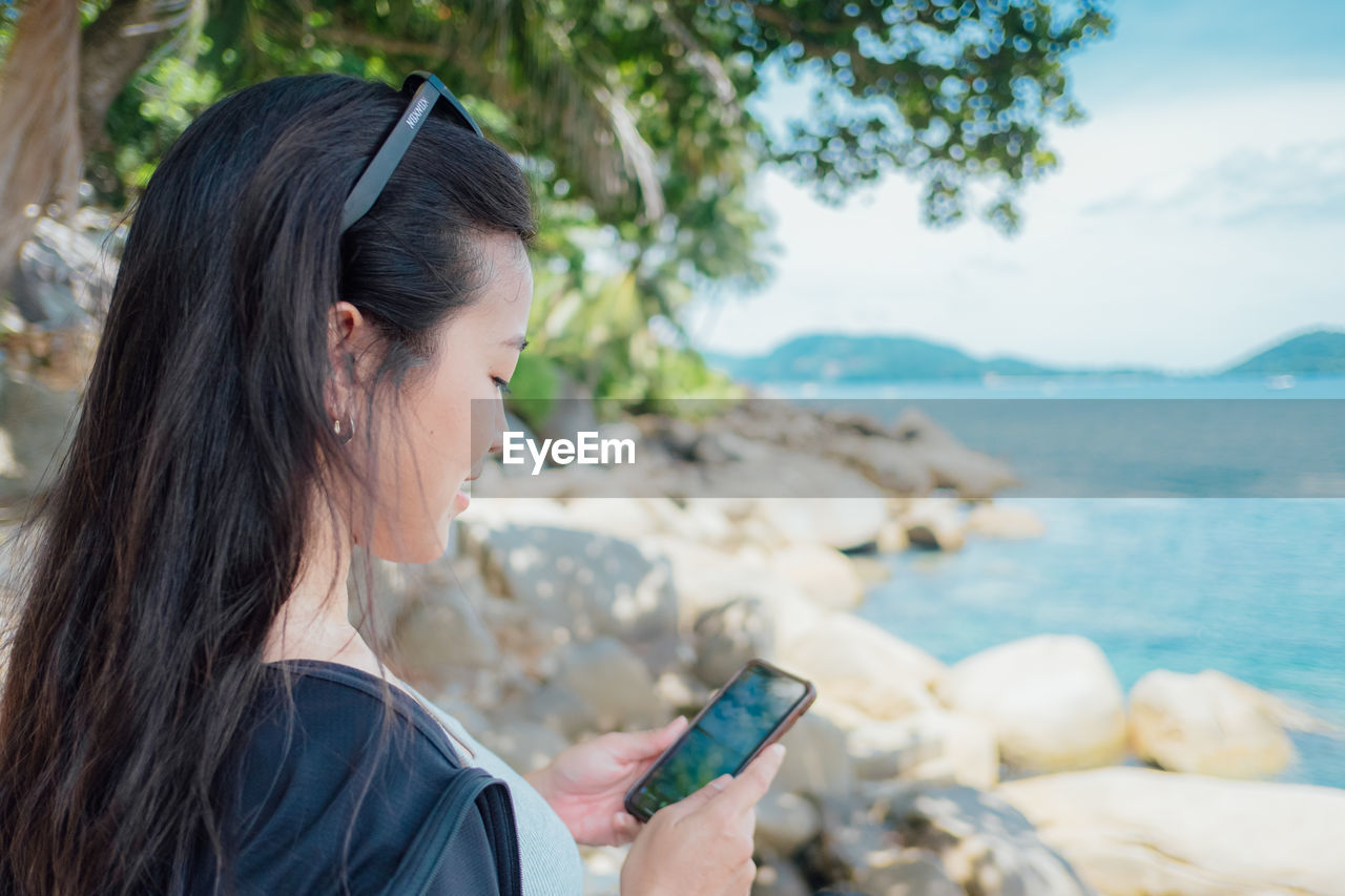 Young woman using mobile phone while sitting at beach