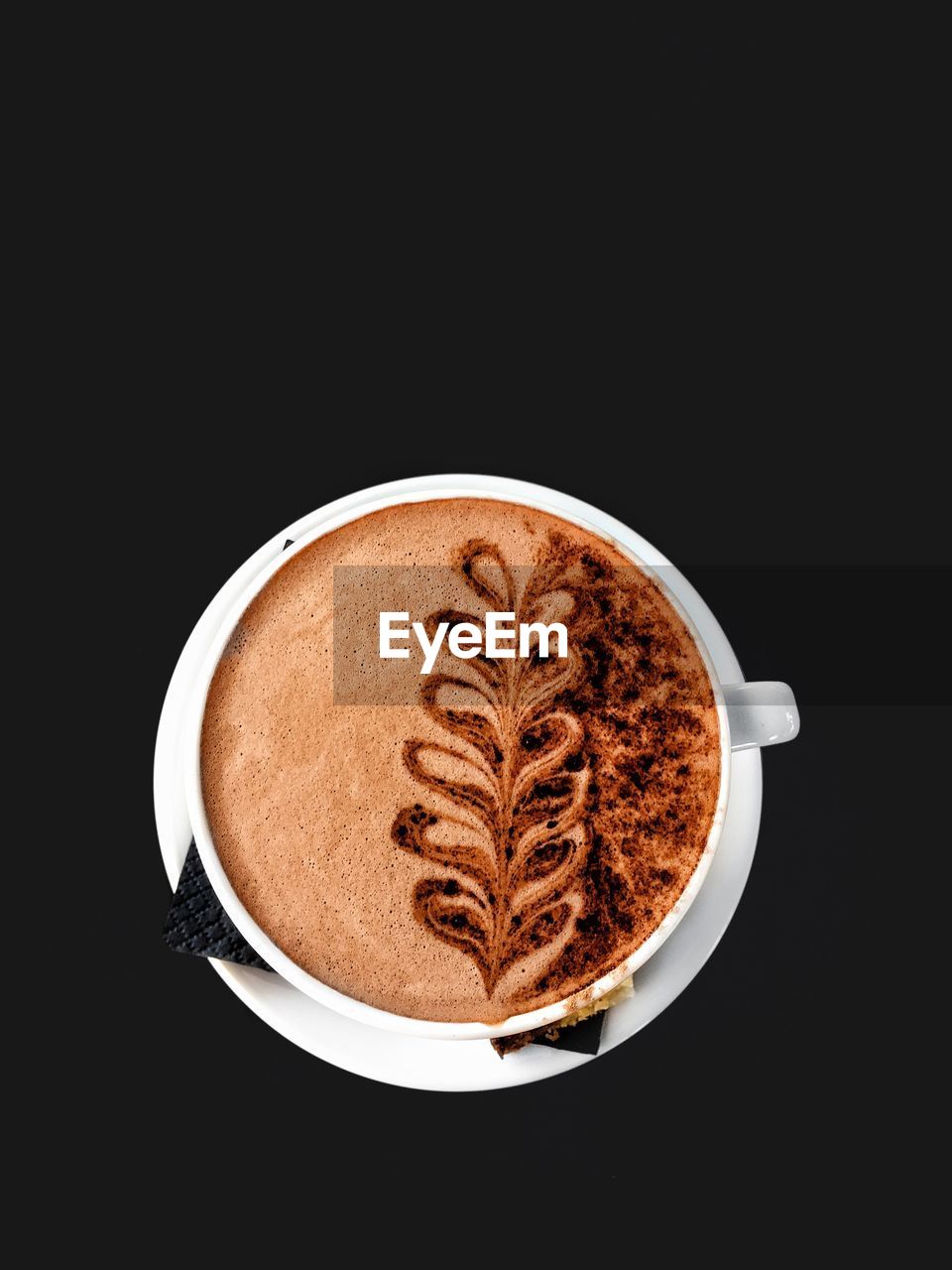 Top view of a white cup of hot chocolate with design on a black background