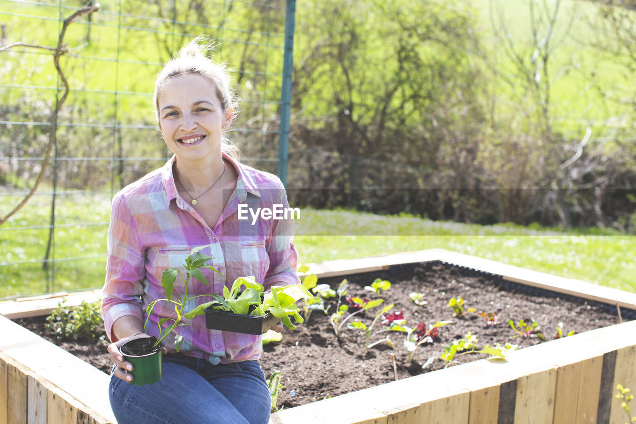 Smiling woman sitting on raised bed in yard