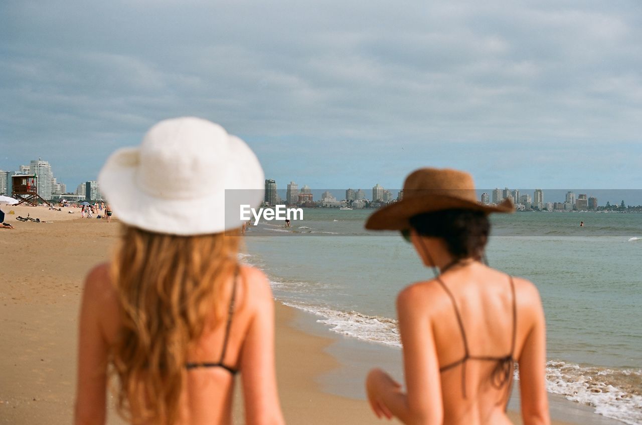 Back view of women standing at beach against sky
