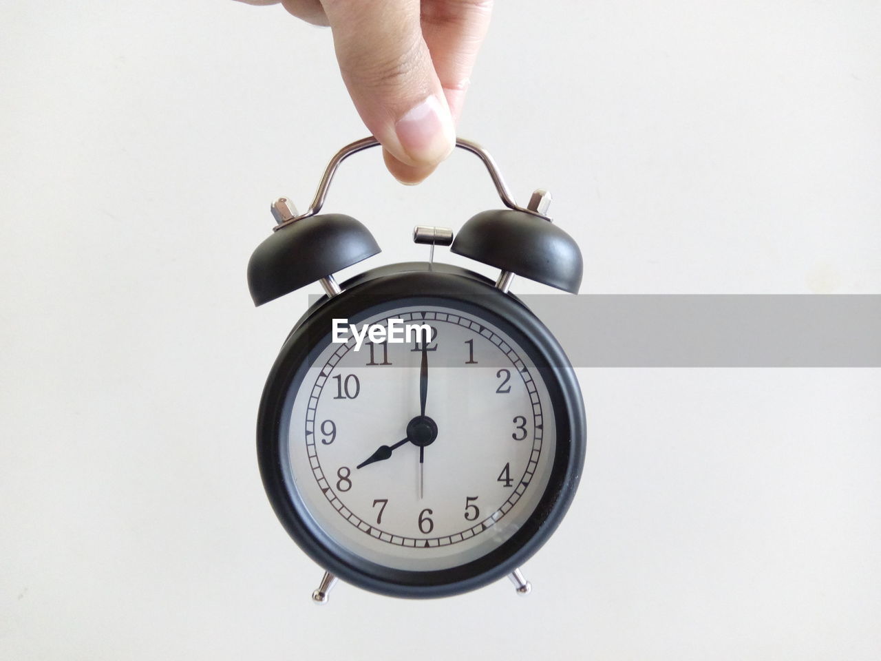 Cropped hand of person holding alarm clock against white background