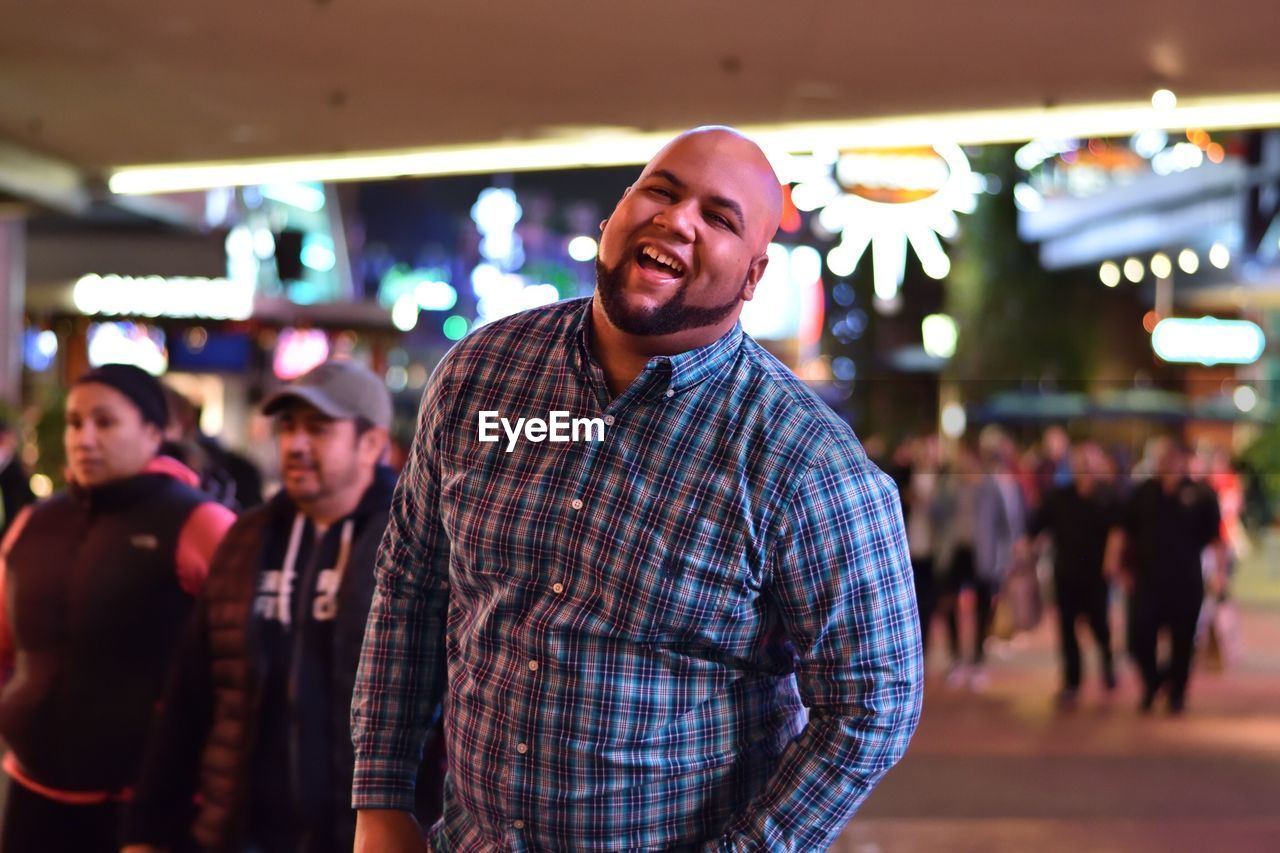 Portrait of cheerful man standing at amusement park during night