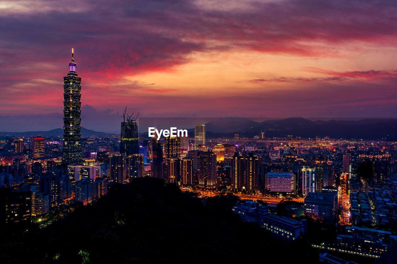 ILLUMINATED BUILDINGS IN CITY AGAINST SKY AT SUNSET