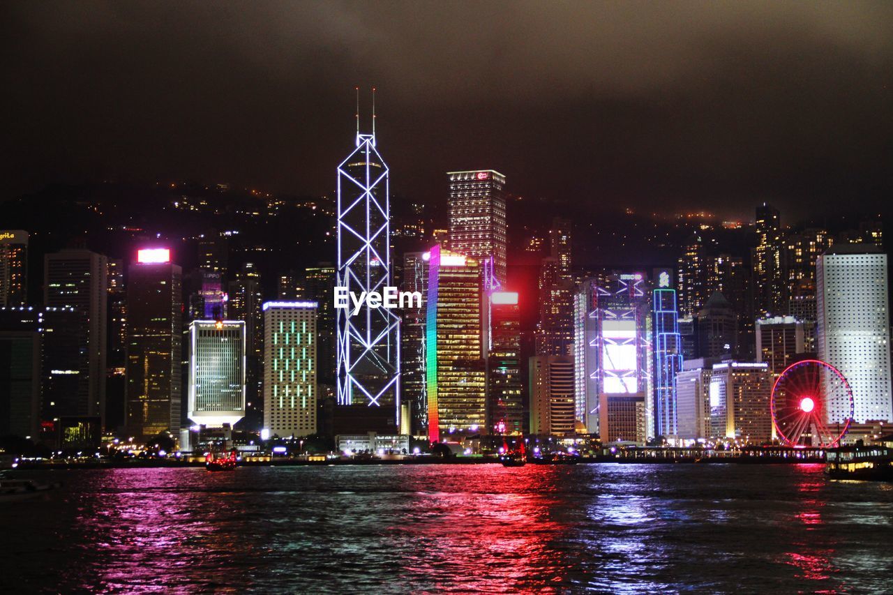 ILLUMINATED BUILDINGS BY RIVER AGAINST SKY