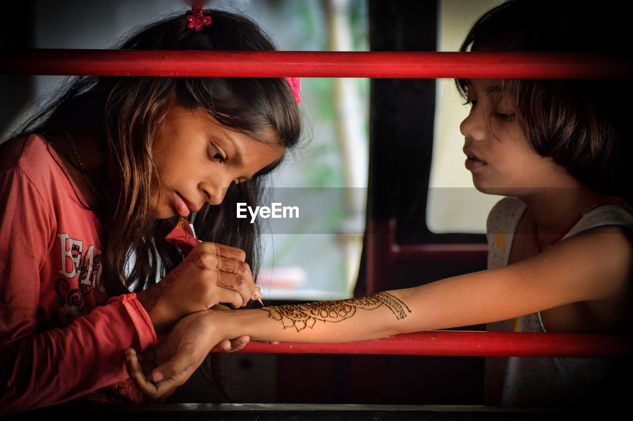 Girl applying henna tattoo on sister forearm