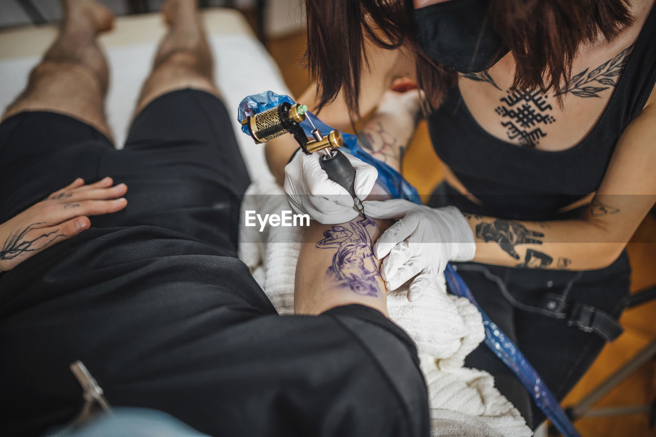 Top view of female tattoo master tattooing mans arm in a studio