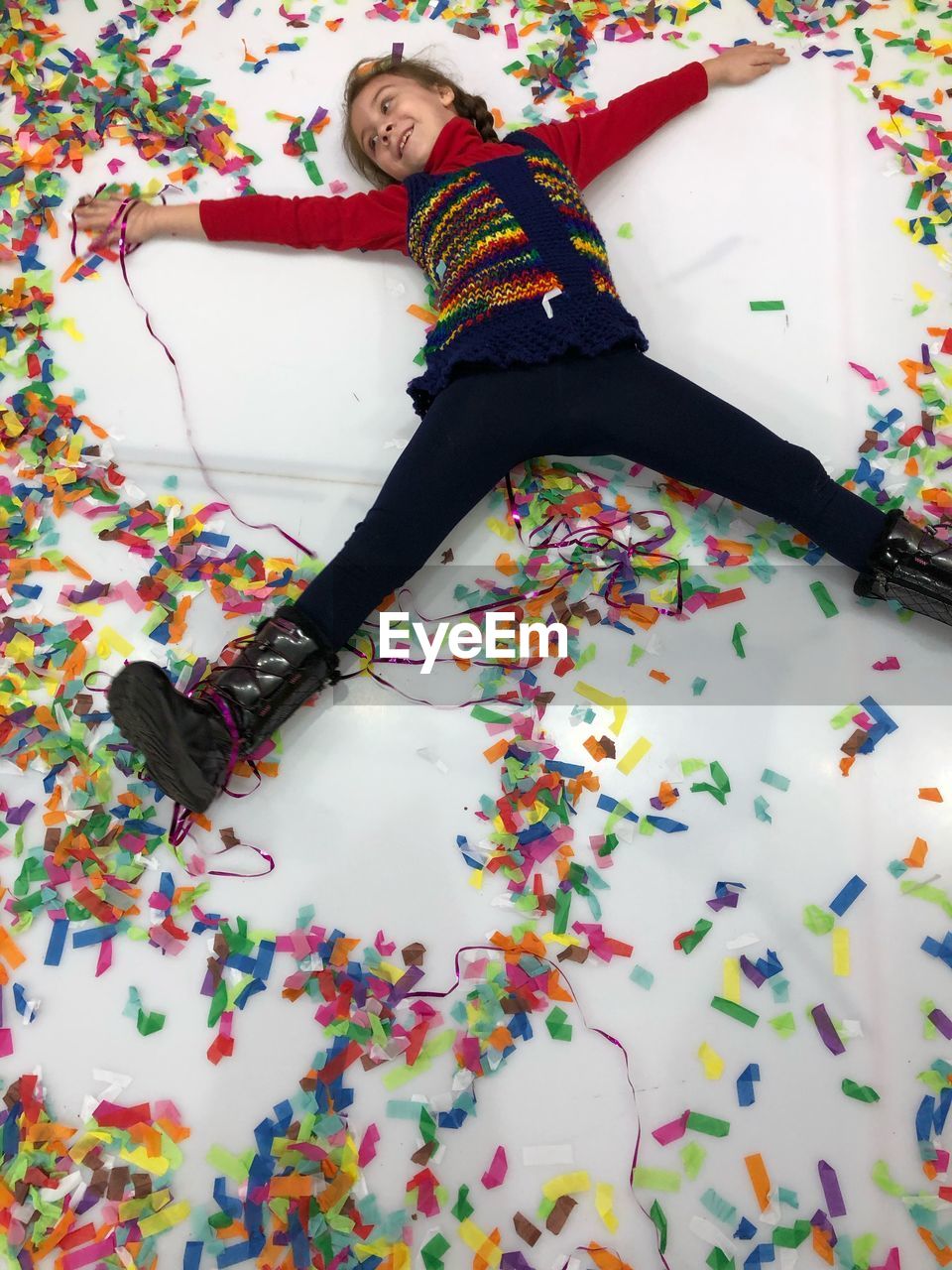High angle view of playful girl with confetti lying on floor at home