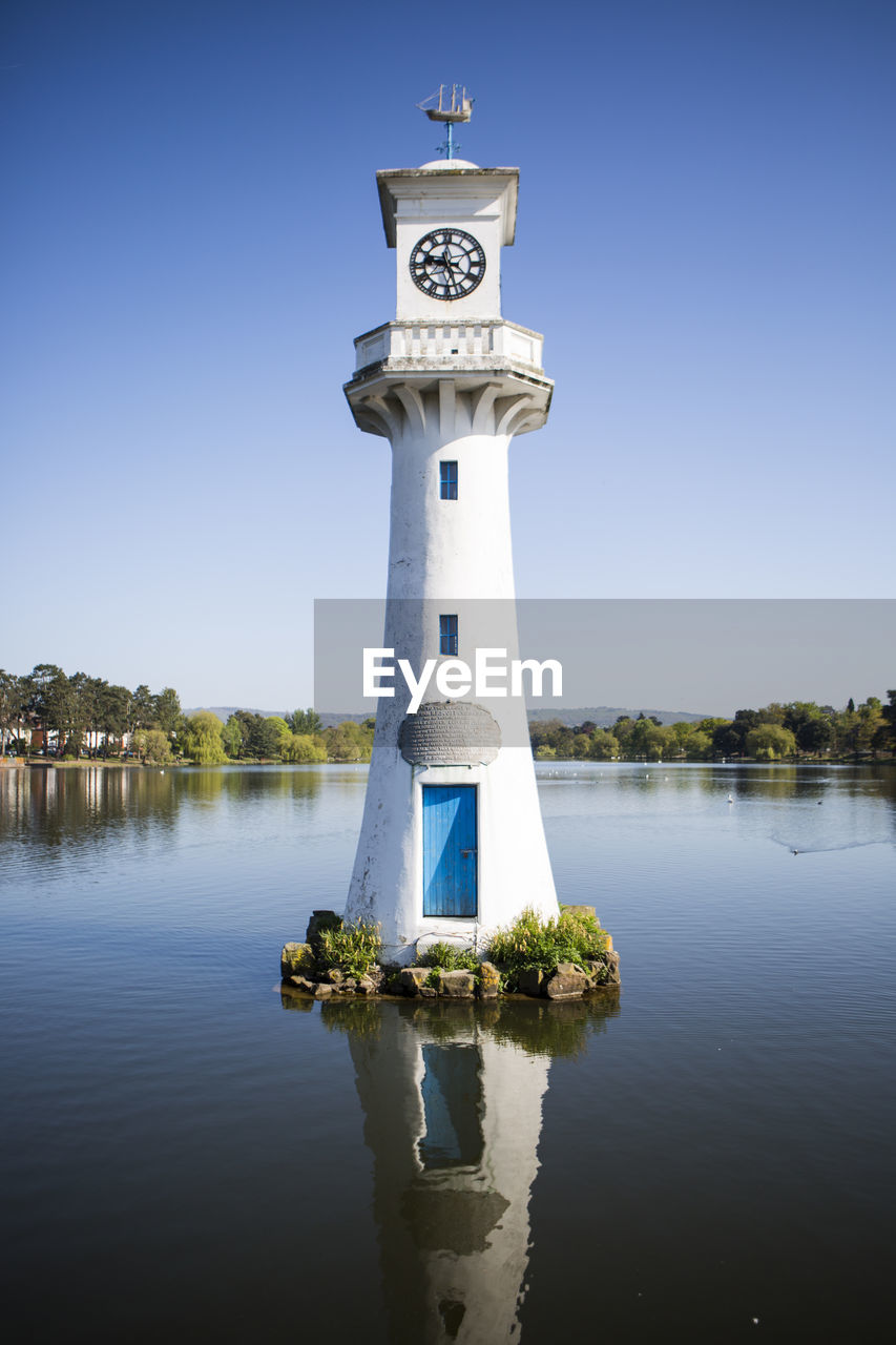 Lighthouse by lake against clear blue sky