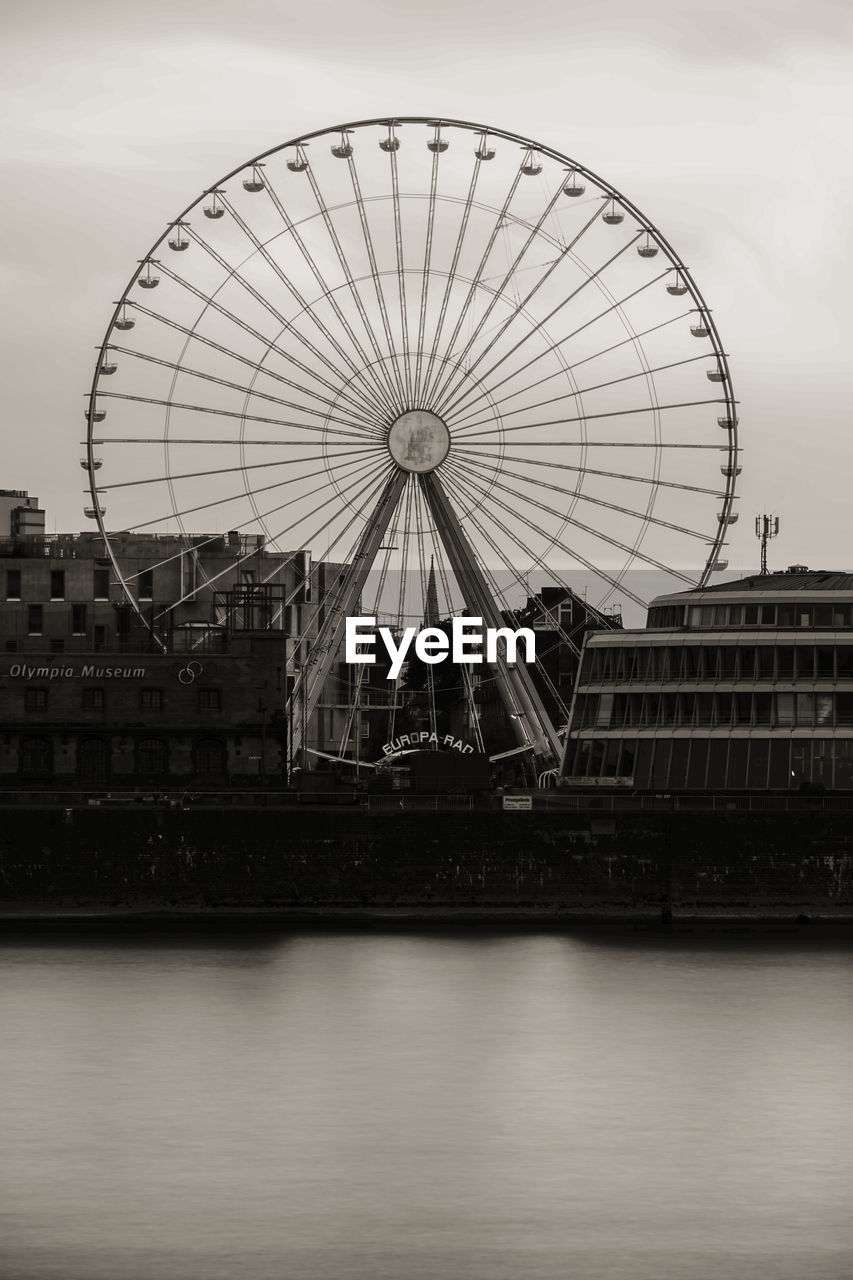 Ferris wheel by river against sky in city