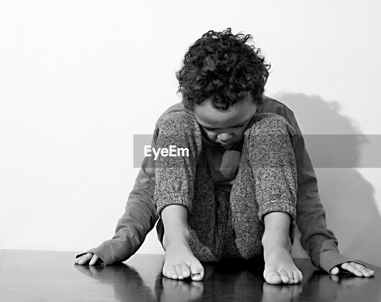 Full length of sad boy sitting on floor against wall