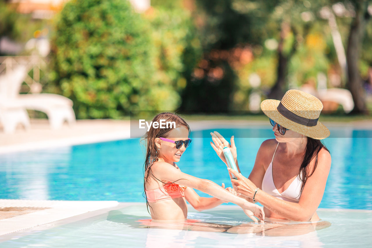 Mother applying sunscreen to daughter in swimming pool