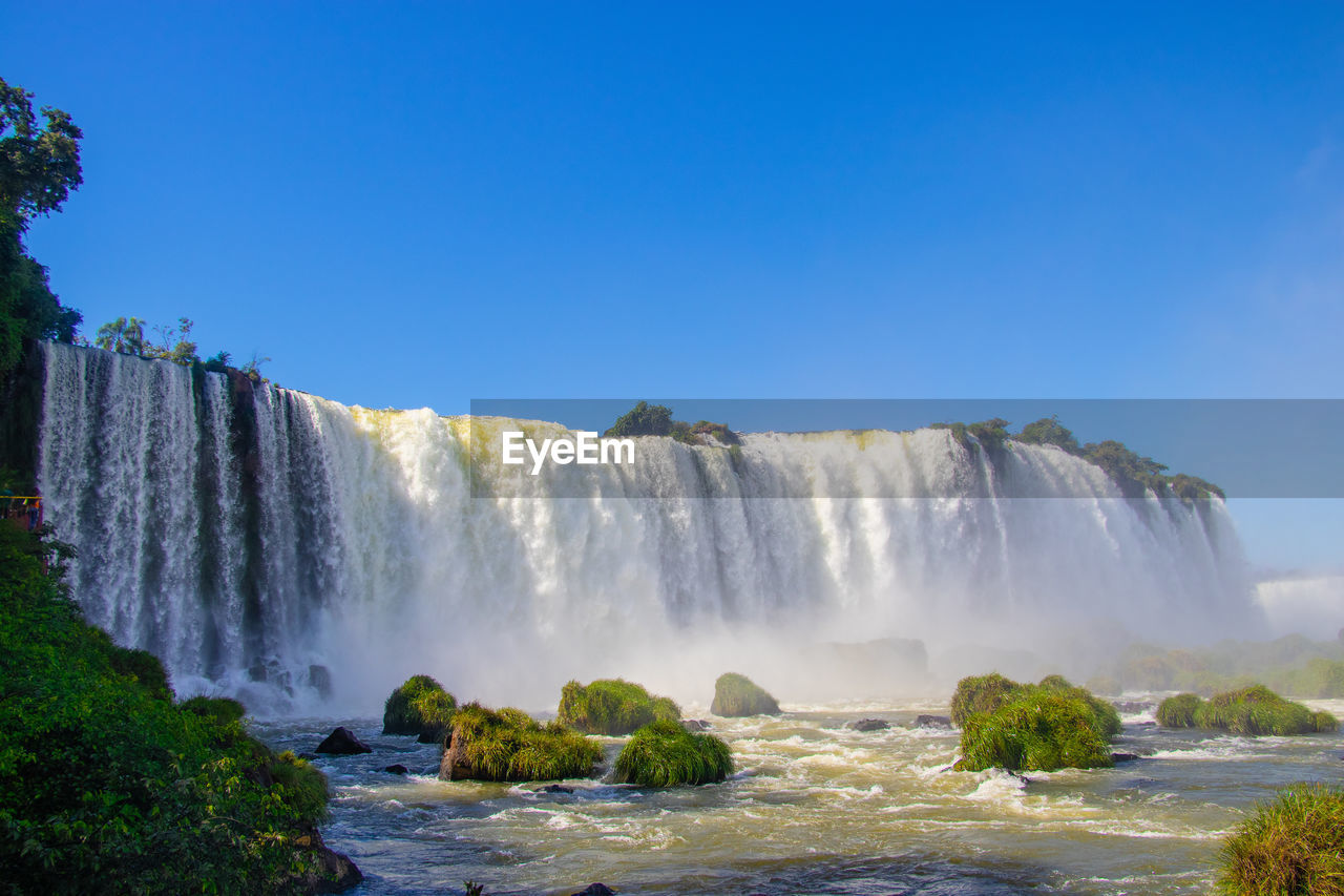 Scenic view of waterfall against blue sky