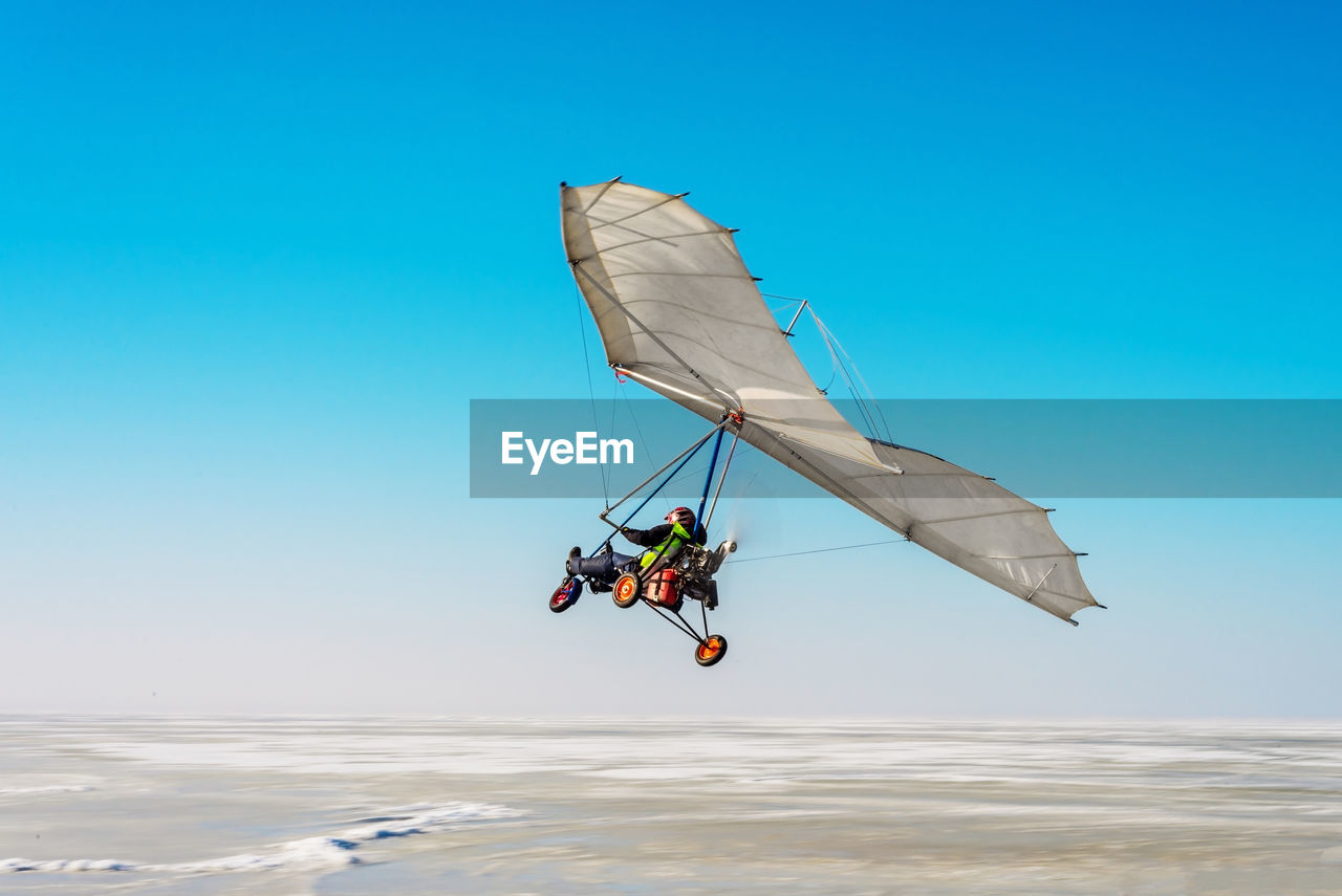 Man paragliding over sea against blue sky