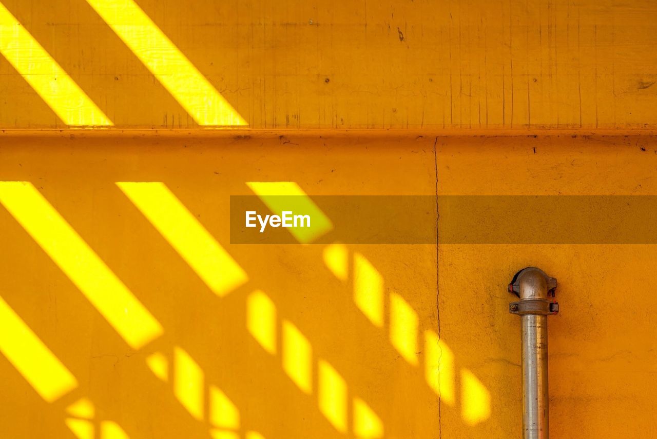 Close-up of cropped railing and sunlight on yellow wall