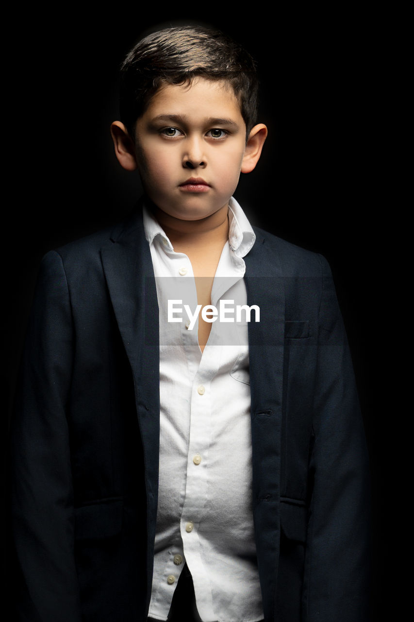 Portrait of boy wearing blazer standing against black background