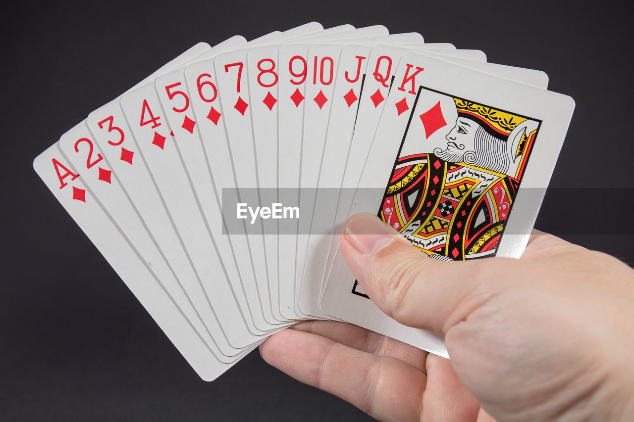 Cropped image of hand holding playing card against black background