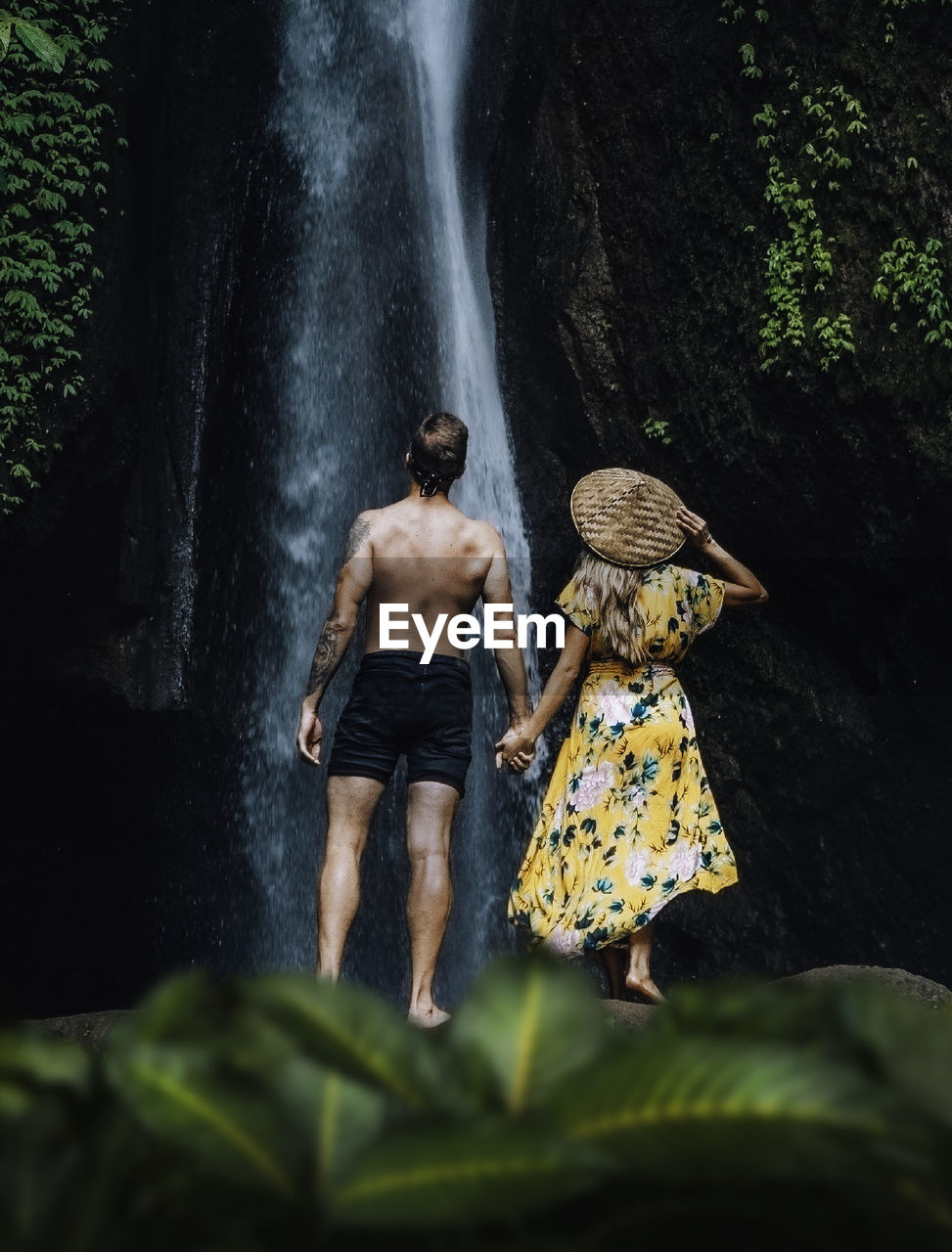 Rear view of couple enjoying waterfall in forest