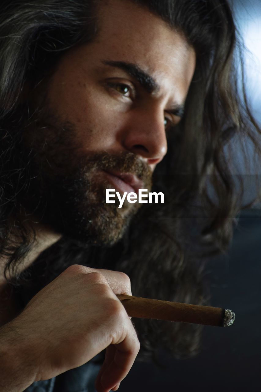 Man looking away while smoking cigar in darkroom