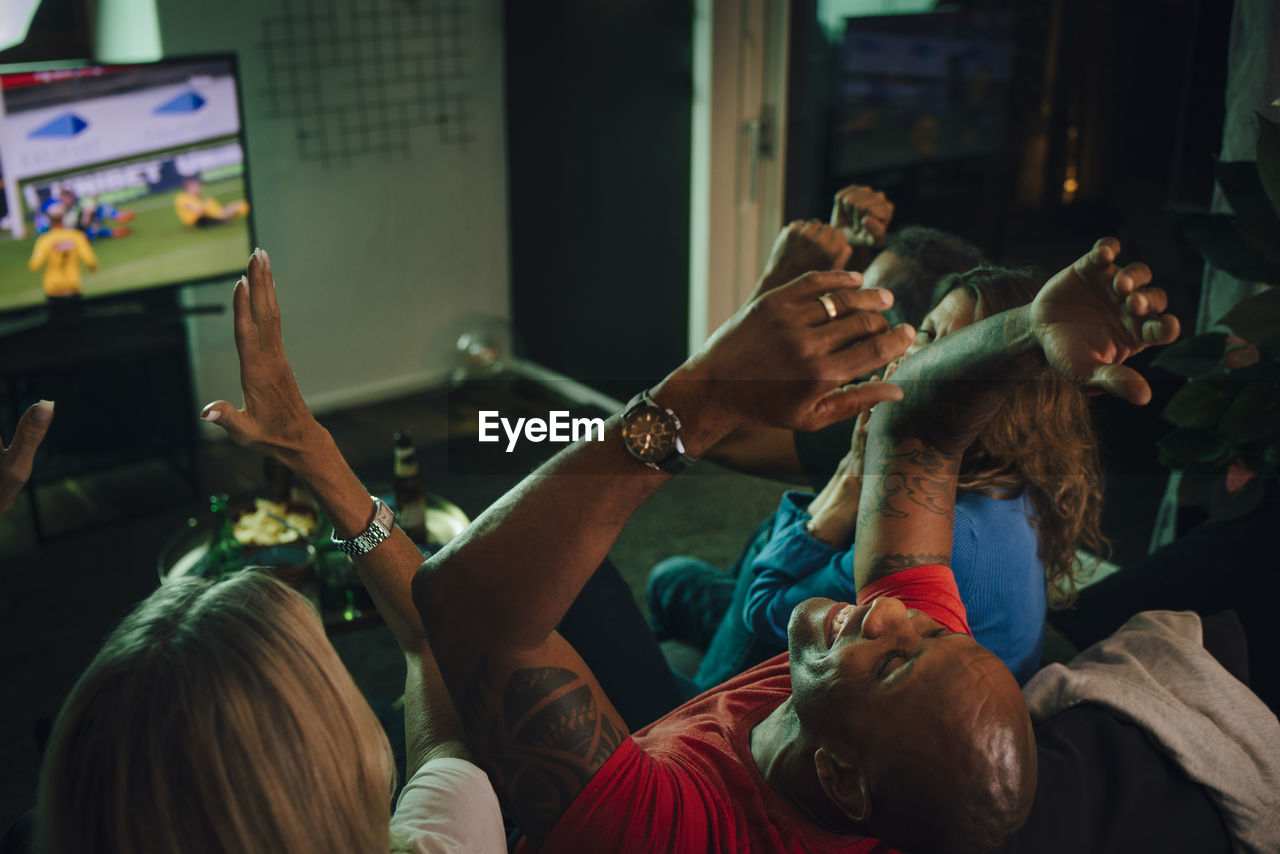 High angle view of friends cheering while watching sports on tv in living room