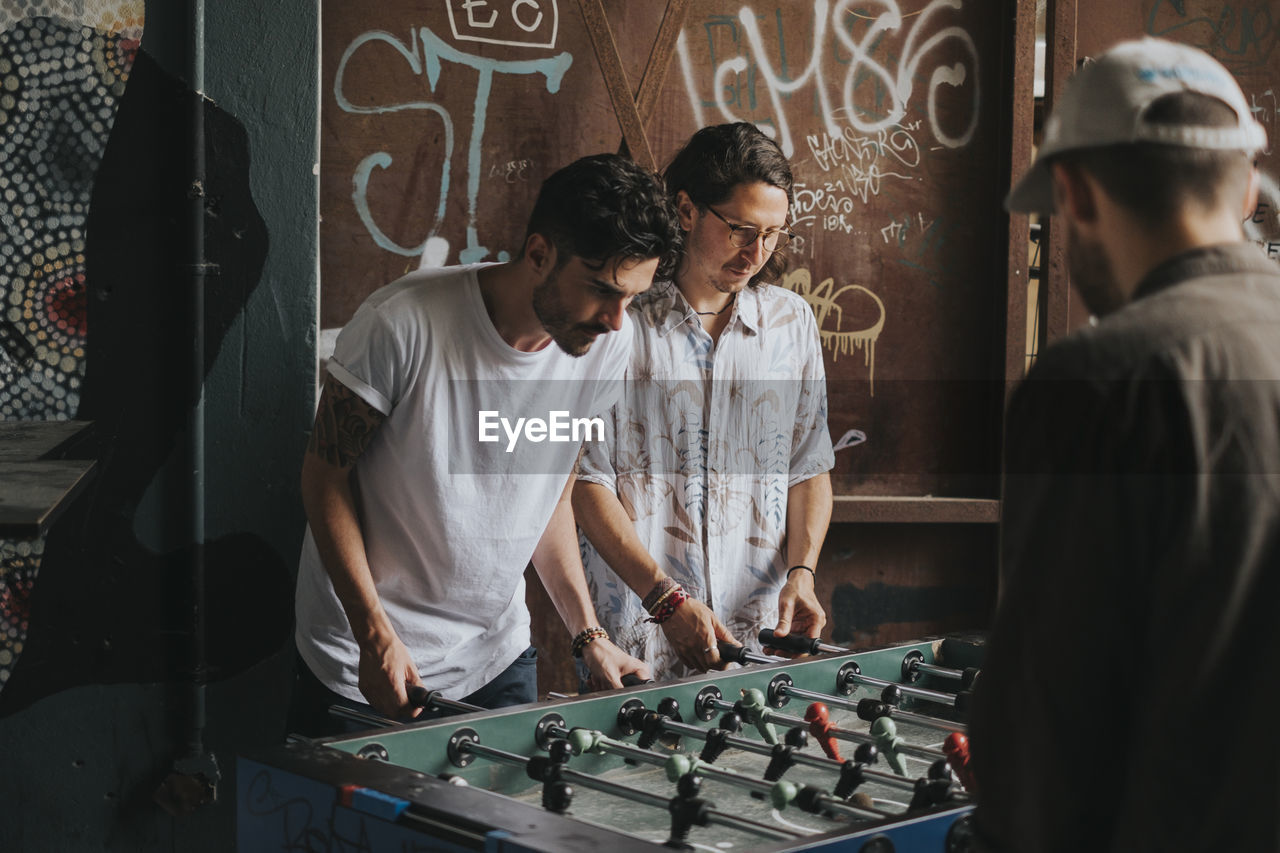 Friends playing foosball against graffiti wall at club