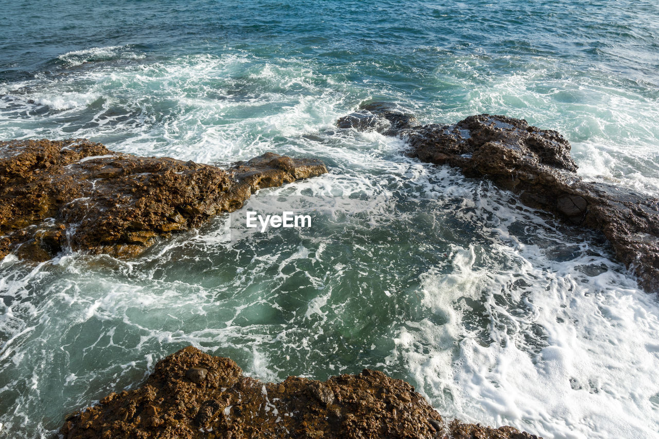 HIGH ANGLE VIEW OF WAVES BREAKING ON ROCKS